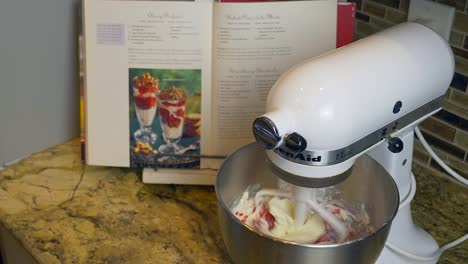 Kitchen-aid-mixer-is-stirring-cream-cheese-and-Raspberries-for-a-dessert-on-a-granite-kitchen-counter