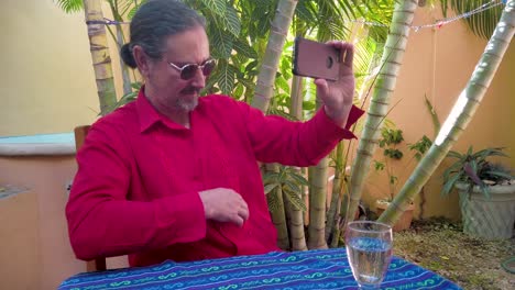 Mature-man-responding-to-someone-on-smartphone,-shows-off-his-guayabera-shirt