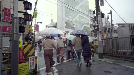 Menschenmenge-Mit-Regenschirm-überquert-An-Einem-Regnerischen-Tag-In-Tokio,-Japan,-Die-Bahnstrecke