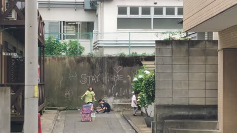 Japanese-Kids-Playing-Next-To-A-Wall-With-STAY-AT-HOME-Written-On-It-During-The-Coronavirus-Pandemic-In-Kyoto,-Japan