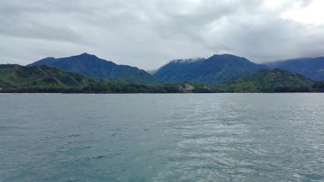 4K-Hawaii-Kauai-Bootfahren-Auf-Dem-Meer,-Das-Von-Rechts-Nach-Links-In-Richtung-Berge-Und-Wolken-Schwimmt,-Mit-Bootsgischt-Im-Vordergrund
