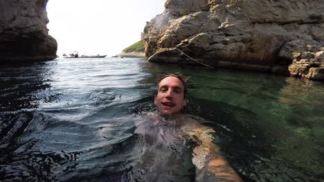 Hombre-Nadando-En-La-Espalda-En-La-Superficie-Del-Agua-Clara-En-Una-Cala-Aislada-De-Hvar,-Croacia-Se-Sumerge-Bajo-El-Agua