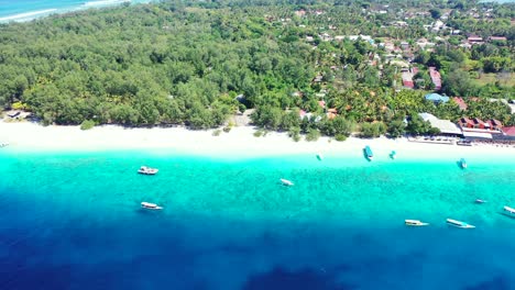 Boats-floating-over-blue-azure-sea,-washing-white-sandy-beach-of-tropical-island-with-lush-vegetation-around-villas,-holiday-resorts-in-Bali