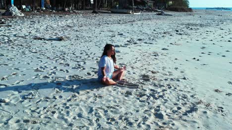 Eine-Frau-Praktiziert-Meditation-Am-Wunderschönen,-Heißen,-Weißen-Sandstrand-Indonesiens,-Während-Die-Wellen-Ans-Ufer-Rollen-–-Totale