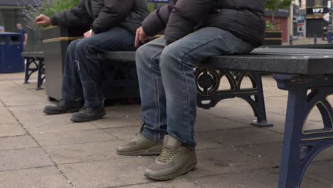 Two-men-sitting-in-town-centre-social-distancing-on-bench-medium-shot