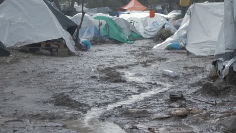 Bleak-low-angle-shot-Moria-Refugee-Camp-tents-in-muddy-inhumane-conditions,-rack-focus-child-blue-poncho