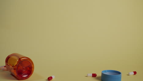 Slow-motion-wide-shot-of-a-bottle-of-pills-falling,-the-lid-flies-off-and-pills-shoot-out