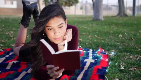 A-hispanic-woman-student-reading-and-studying-a-school-textbook-on-a-college-campus-at-sunset