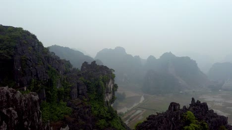 The-limestone-karst-eroded-mountains-of-Tam-Coc-on-Ninh-Binh-province-Vietnam-during-foggy-day,-Aerial-pan-left-shot
