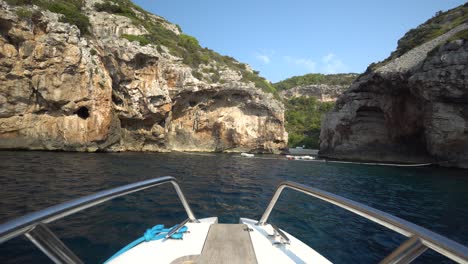 Bow-of-small-boat-headed-toward-steep-cliffs-that-conceal-a-hidden-exclusive-beach-on-an-island-in-Croatia