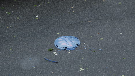 Trash-Can-Lid-Is-Ran-Over-In-The-Street-By-Car-During-a-Rainstorm