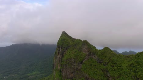 Vista-Aérea-De-Un-Pico-Montañoso-Cubierto-De-Vegetación-Y-Nubes-De-Baja-Altitud-En-La-Polinesia-Francesa