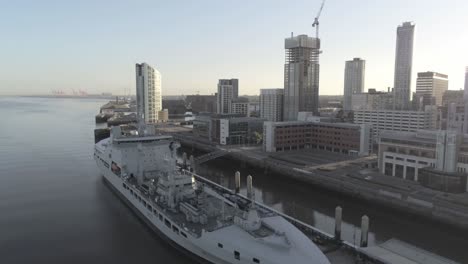 Liverpool-waterfront-aerial-view-royal-navy-military-ship-sunrise-high-rise-buildings-skyline-descend-right