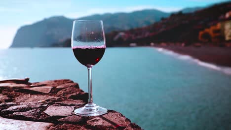 Red-wine-poured-into-wine-glass-overlooking-beach-with-mountains,-Madeira