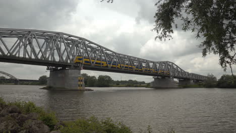 Two-train-passing-over-the-railbridge-at-Hedel,-crossing-the-Maas-river