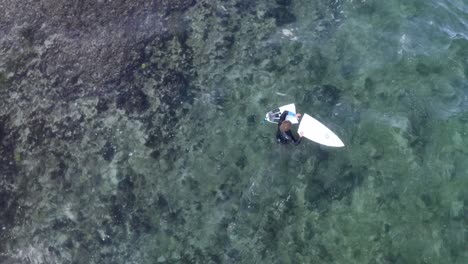 Male-surfer-exiting-rocky-patch-at-Balangan-Beach-with-his-broken-board-in-two-pieces,-Aerial-top-view-shot