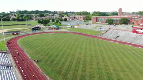 Student-athletes-socially-distanced-at-practice,-gym-class-on-university-school-running-track,-aerial-view