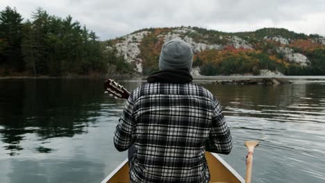 Man-plays-Ukelele-in-a-Canoe-in-Autumn-Leaf-Color-Forest-on-Canada-lake