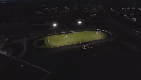 Aerial-footage-of-a-football-field-stadium-with-lights-on,-4k-drone