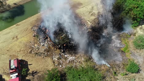 Aerial-view-of-a-firefighter-trying-to-calm-a-building-fire,-smoke-rising-at-a-river-on-the-countryside,-of-Mexico,-Central-America---static,-drone-shot