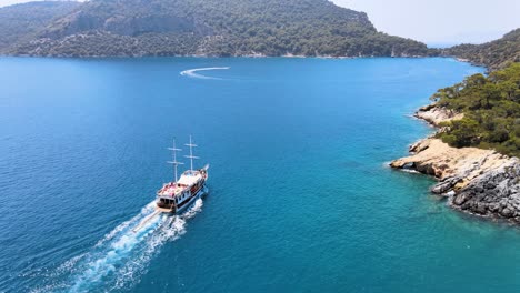 Drone-fly-over-a-bay-in-the-Mediterranean-over-a-yacht-sailing-between-islands-covered-in-green-trees-under-a-blue-sky