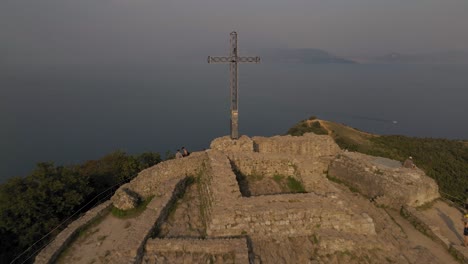 Steel-cross-with-graffiti-details-and-Lake-Garda-in-the-mist-aerial-panorama