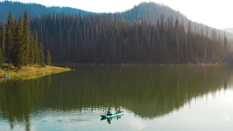 Aerial-shot-of-a-man-and-his-two-daughters-fishing-in-a-canoe-on-a-mountain-lake-during-golden-hour