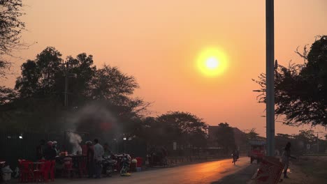 Time-Lapse-of-a-Sunset-on-a-Busy-Street-with-a-Street-Food-Stall-Preparing-Food-and-Selling-it-on-The-Roadside-and-Many-Vehicles-Going-Past