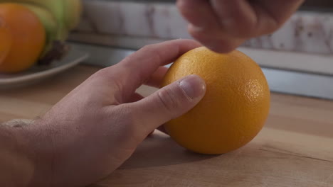 Die-Hand-Eines-Mannes-Schneidet-Orangefarbene-Früchte-Mit-Einem-Messer-Auf-Einem-Hölzernen-Schneidebrett
