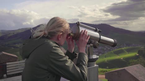 Ein-Blondes-Mädchen-In-Einem-Grünen-Regenmantel,-Das-Durch-Ein-Teleskop-Ins-Tal-Blickt