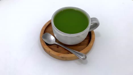 Hot-brewed-fresh-green-tea-served-in-a-cup-with-spoon-on-wooden-table-with-white-background