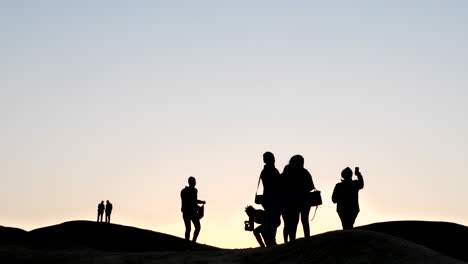 Wide-shot-of-people-in-silhouette-against-a-pink-sky-in-the-Namib-desert-at-sunset