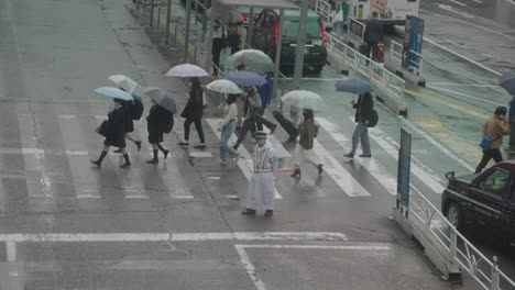 Japanese-High-School-Students-Holding-Umbrellas-Up-Crossing-The-Road-Near-A-Taxi-Stand-On-A-Rainy-Day-In-Shibuya,-Tokyo,-Japan