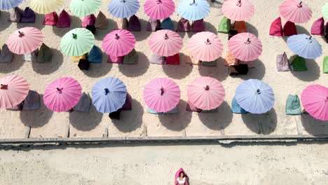Aerial-top-down-view-of-young-girl-lying-at-beach-during-summertime-in-front-of-colorful-umbrellas