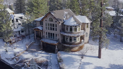 Warm-Christmas-welcome-home-winter-Big-Bear-California-aerial,-Snow-Covered-Mansion-surrounded-by-trees