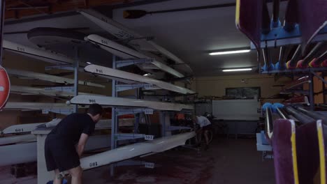 Two-men-putting-kayak-on-storage-rack-shelf-indoors,-Slow-Motion