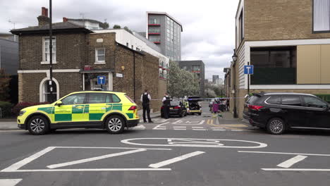 People-walk-past-a-paramedic-car-parked-next-to-a-police-cordon-crime-scene-where-police-officers-operate-following-a-stabbing-incident
