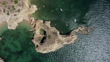 Top-Down-Birdseye-view-of-epic-ocean-cliffs-surrounded-by-reflective-green-waves,-drone-aerial