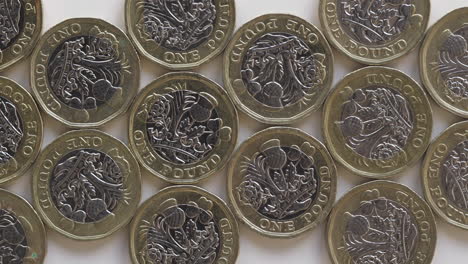 British-One-Pound-Coins-Engraved-With-Iconic-Floral-Design-Flat-Lay-On-White-Table---Closeup-Slider-Shot