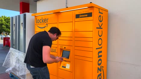 A-man-picking-up-a-package-at-the-Amazon-hub-Locker-pick-up-point-in-Spain,-4K-static-shot