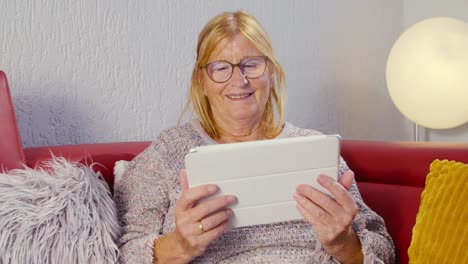 Ältere-Frau-Schaut-Auf-Ein-Tablet-Und-Lächelt-Nach-Draußen