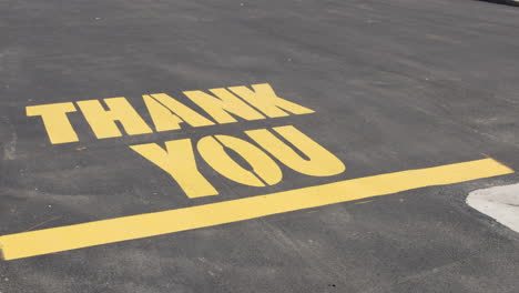 Still-shot-of-Thank-You-message-lettering-in-yellow-paint-on-blacktop-surface