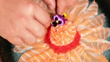 Adding-Colorful-Flowers-As-Decoration-To-A-Platter-Of-Delicious-Salmon-Sashimi-With-Roe---close-up