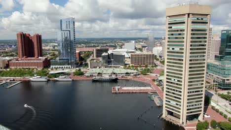 Cinematic-aerial-turn-reveals-Baltimore-financial-district-above-Inner-Harbor,-clipper-ship,-skyscrapers,-sunny-summer-day