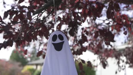 Close-up-tracking-shot-of-a-creepy-Halloween-ghost-decoration-hanging-on-a-blossom-tree-in-Autumn-and-swaying-with-the-wind