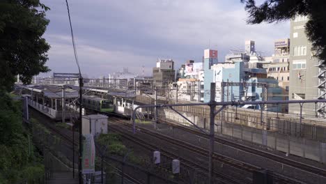 Multiple-trains-including-Shinkansen-driving-past-train-station-in-typical-Japanese-Urban-city---wide-view