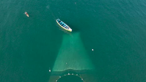 Aerial-top-down-view-of-fisherman-boat-with-the-fishnet-being-laid-over-the-surface-of-water-for-catching-fish