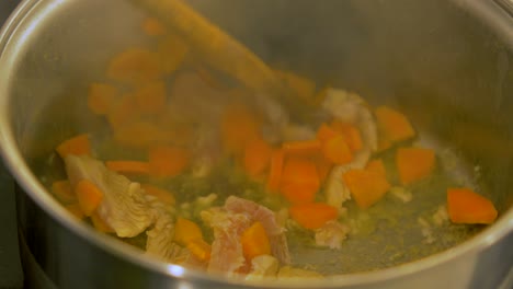 The-cook-mixes-chicken-and-fresh-cut-carrots-in-the-steel-pot,-making-pasta-salad,-handheld-close-up-shot