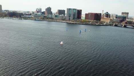 Aerial-View-Of-Sailboats-In-Charles-River-With-Boston-Cityscape-From-Cambridge,-Massachusetts---drone-shot---out-of-focus