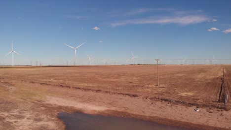 Drone-shot-of-spinning-wind-turbines,-electric-poles-in-a-dry-area
